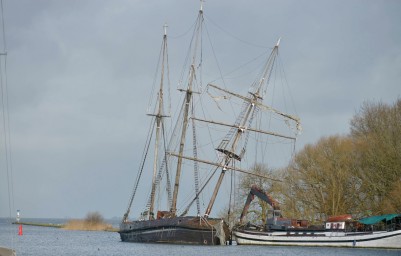 Het schip ligt tegen de vaargeul van het Markermeer nabij de sluis van Muiden. Door wind, weer en water geteisterd zijn de masten de afgelopen week verder uit het lood gezakt. (foto E.J. Bruinekool Fotografie)